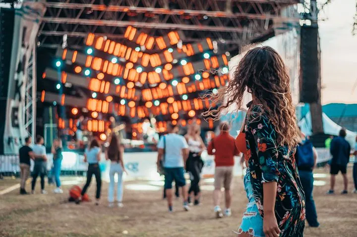 A woman walking towards a lit outdoor festival stage at dusk